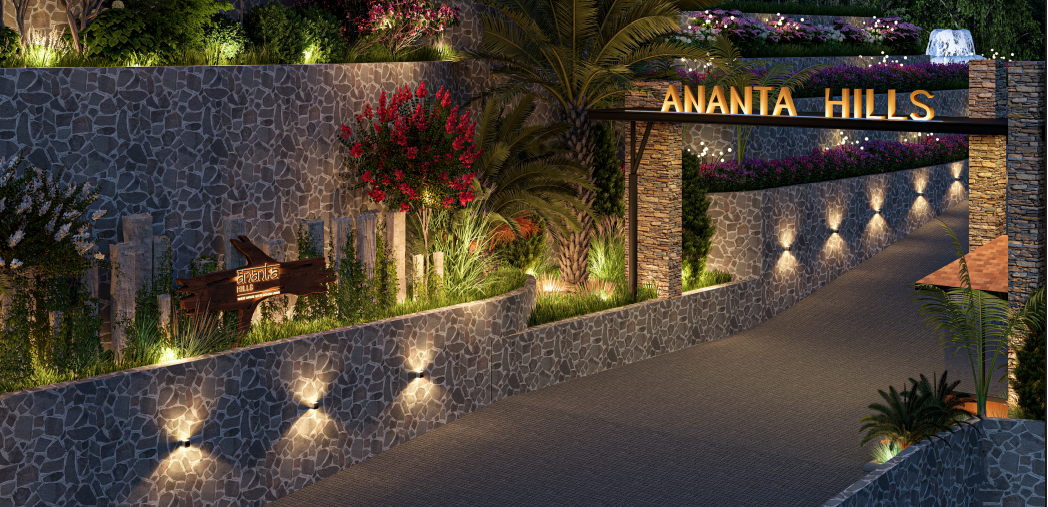 "Night view of the illuminated grand entrance gate at Ananta Hills Dehradun, featuring stone cladding, modern signage, and landscaped stone walls in a premium gated community."